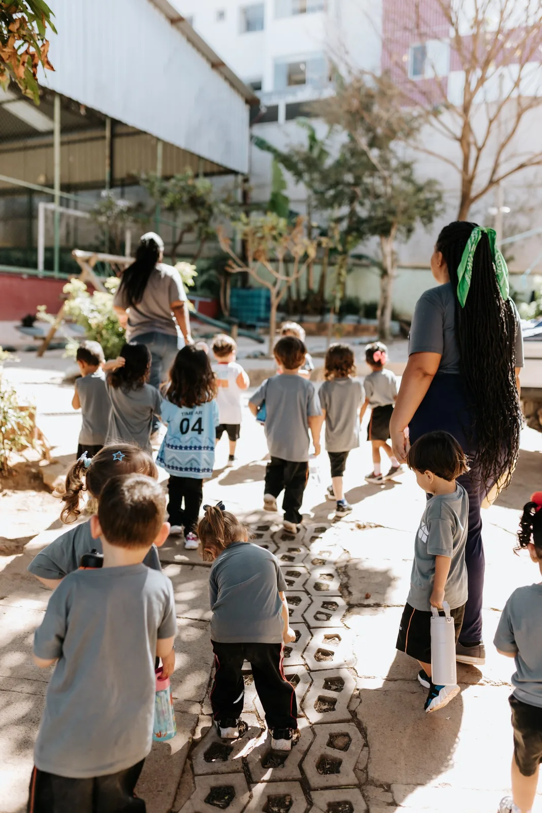 Crianças da Educação Infantil caminhando pelo pátio com educadoras